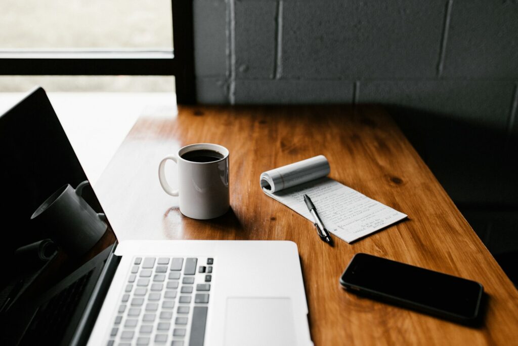 Laptop, Notizbuch und Kaffeebecher auf einem Schreibtisch