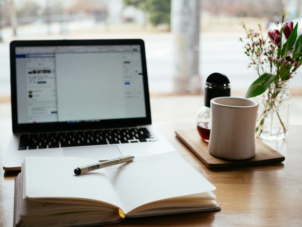 Berufliche Weiterbildung: Laptop neben aufgeschlagenem Fachbuch auf einem Schreibtisch